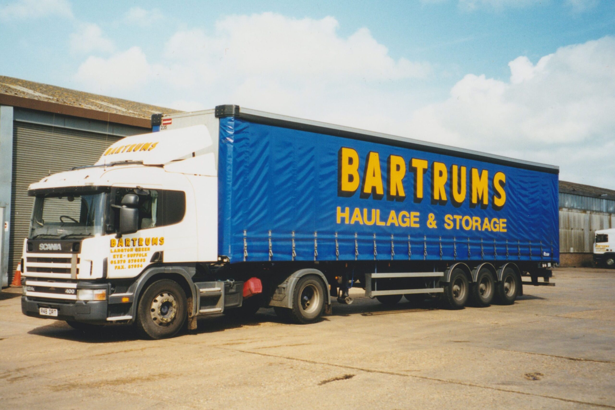 A coloured photograph of a Bartrums lorry. The lorry is blue, with large yellow text on the side.