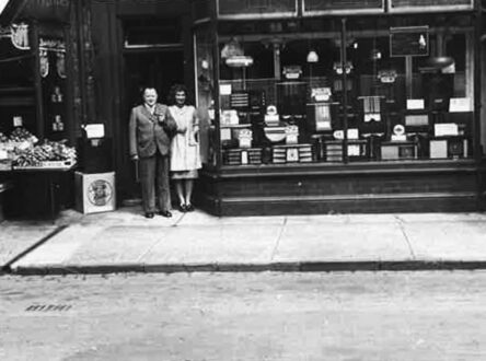 An old black and white photo of a man and woman standing in a doorway of a shop.