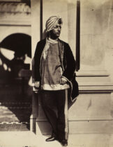 A man of South Asian in a turban standing next to a building.