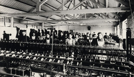 A black and white photograph of women working at a large loom.