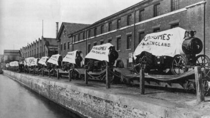 A black and white photograph of old vehicles lined up on a dockside.