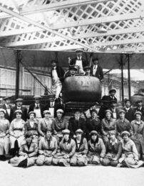 A black and white photograph of men and women in front of a bi-wing aircraft.