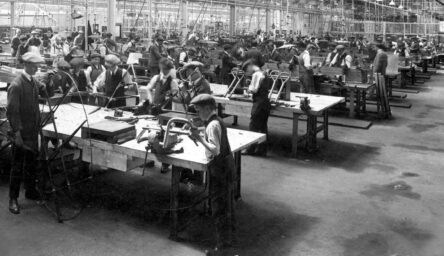 A black and white photograph of boys and men in flat caps working in a factory.