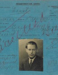 An old blue postcard size document with faded black and red handwriting, and a passport image of a man dressed in a suit and tie.