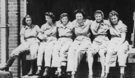 A black and white photograph of six women sitting on a wall.