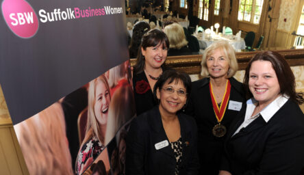 A photograph of four women in front of a banner stand.