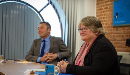 A white man and white woman sit at desk in a meeting.
