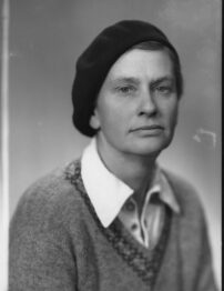 Black and white portrait photo of a woman wearing a dark coloured beret, a white shirt and v-necked jumper.