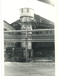 A black and white photo of a industrial tower within a factory setting.