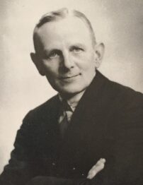 Black and white protrait of a white man in a dark suit.