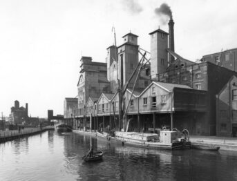 Black and white photograph of a factory on a dockside.
