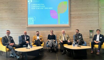 A group of seven people sitting underneath a display screen.