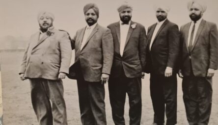 Black and white photo of 5 brown men in suits standing in a line. They are serious, looking into the camera and wearing turbans.