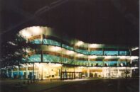 A photograph of a modern office building lit up at night.