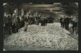 Black and white photograph of men surrounding a large pile of fish at a market.