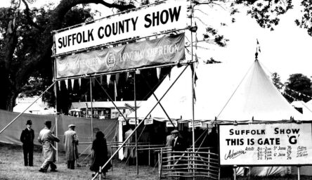 A black and white photograph of a fair ground with large white tents.