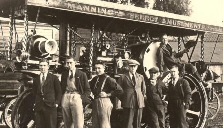 A black and white photograph of seven white men in front of old amusement ground equipment.