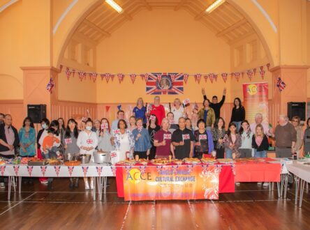 A large group of people, from diverse backgrounds, standing at a party. There is bunting hanging and a flag.