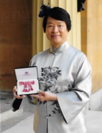 An east Asian woman standing for a portrait with boxed medal in her hand.